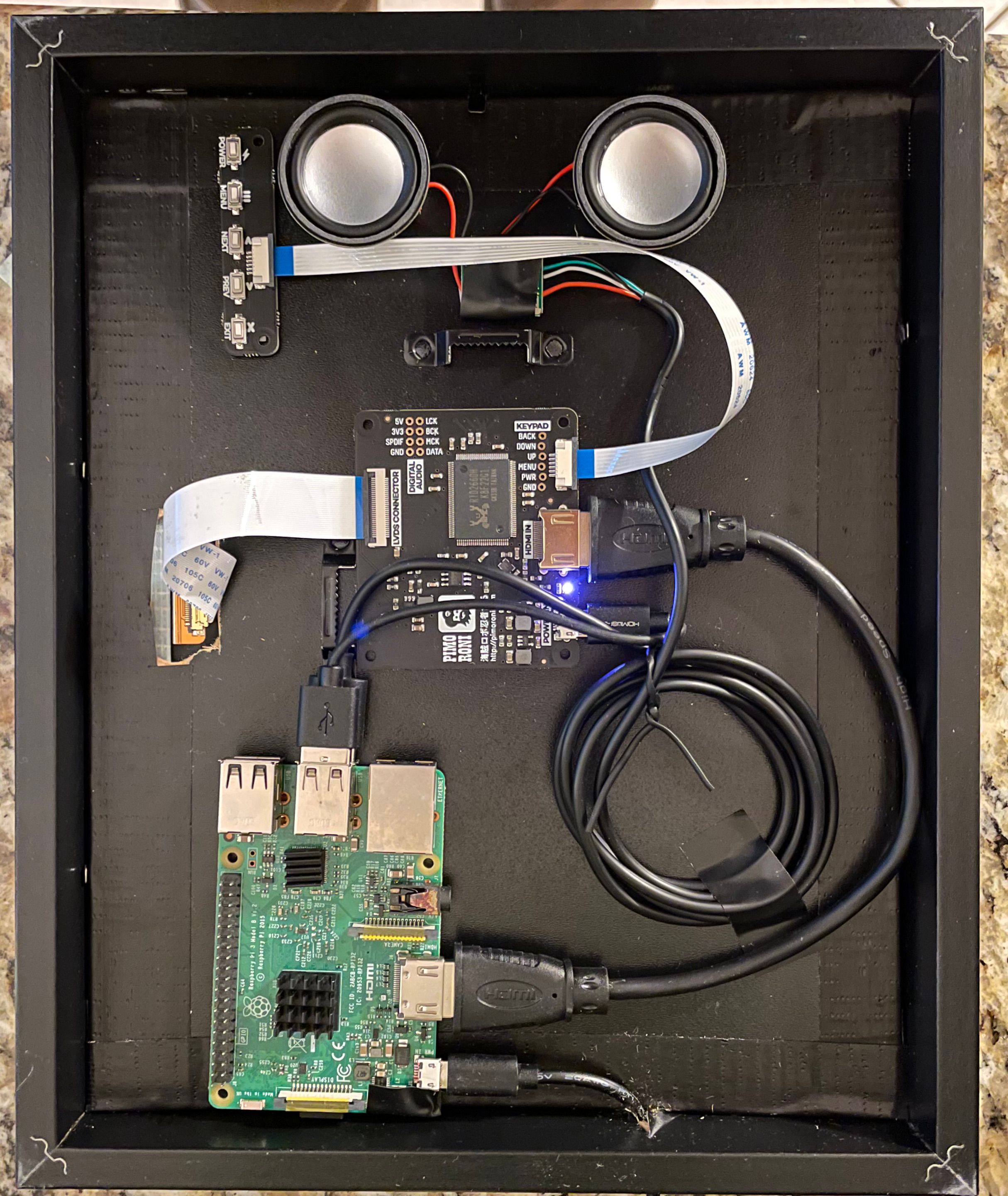 The wiring behind the picture frame; a Raspberry Pi hooked up to a display driver, whose ribbon runs through the back of the frame to the front